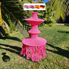 a pink object with tassels on it sitting in the grass next to palm trees