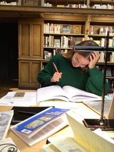 a woman sitting at a table in front of a bookshelf holding a pen and talking on the phone