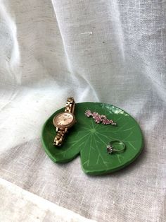 a green leaf shaped tray with two watches on it and some other jewelry laying around