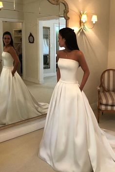 a woman standing in front of a mirror wearing a white wedding dress and looking at her reflection