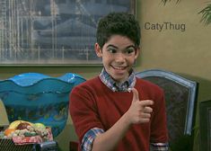 a young boy giving the thumbs up sign in front of a table with fruit and vegetables on it