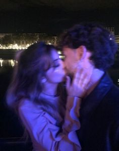 a man and woman kissing in front of the eiffel tower at night time