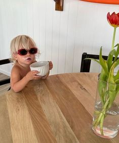 a small child wearing sunglasses sitting at a table with a bowl and flower in it