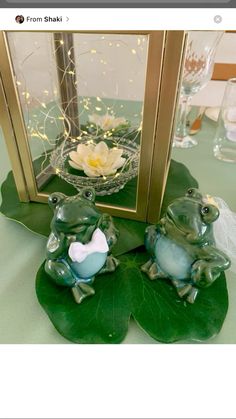 two frog figurines sitting next to each other on a green table cloth with a gold framed mirror behind them