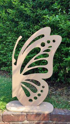 a metal butterfly sculpture sitting on top of a stone block in front of some bushes