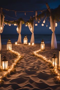 an outdoor wedding setup with lanterns and candles on the sand by the ocean at night