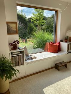 there is a window seat in the living room with books on it and plants outside