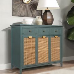 a green cabinet with wicker drawers and a lamp next to it on top of a hard wood floor