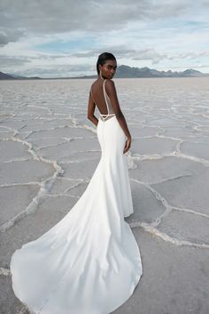 a woman in a long white dress standing on the cracked out ground with her back to the camera