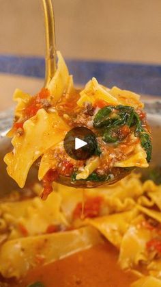 a spoon full of pasta with sauce and spinach on it, being held up by a ladle