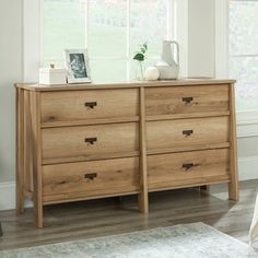 a wooden dresser sitting in front of a window next to a white rug on top of a hard wood floor