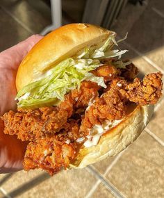 a hand holding a chicken sandwich with lettuce and tomato sauce on the side