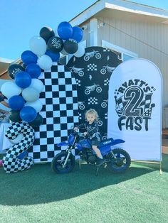 a young boy is sitting on a small motorcycle in front of a race themed backdrop