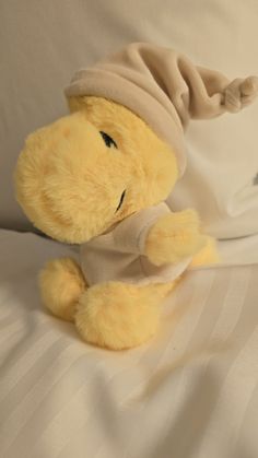 a yellow stuffed animal wearing a hat on top of a white bed sheet and pillows