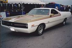 a white and brown car parked in front of a tent with people standing around it