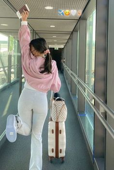 a woman in white pants and pink sweater walking down a hallway with two suitcases