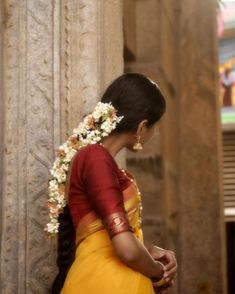 a woman in a yellow and red sari with flowers in her hair standing next to a pillar