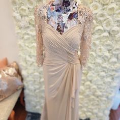 a dress on display in front of a flower wall with white roses behind the mannequin