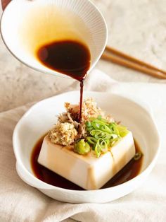 someone pouring sauce on food in a white bowl