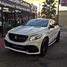 a white mercedes suv is parked in front of a building with an advertisement on it