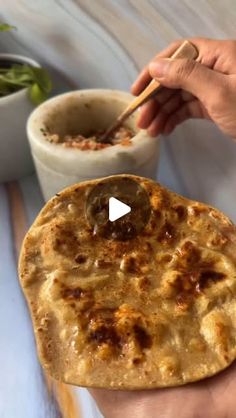 a hand holding a flat bread with a bowl of salad in the background and a video player's thumb pointing at it