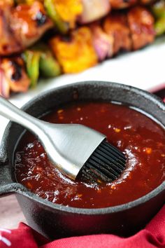 a skillet with sauce and a brush in it on a red towel next to skewers of chicken wings