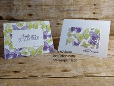 two cards with butterflies on them sitting next to each other in front of a wooden background