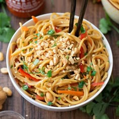 a white bowl filled with noodles, peanuts and carrots on top of a wooden table