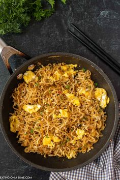 a skillet with noodles and eggs in it next to chopsticks on a table