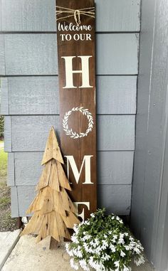 a wooden sign that says welcome to our home next to a potted christmas tree