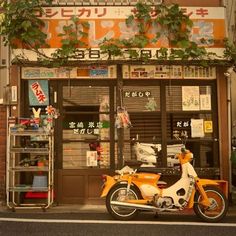 an orange and white motorcycle parked in front of a store with plants growing on the windows