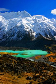 there is a mountain that has snow on it and blue water in the foreground