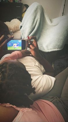 a woman laying on top of a bed holding a cell phone in her hand while playing a video game