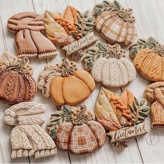 many decorated cookies are sitting on a white wooden table with leaves and pumpkins around them