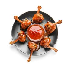 a black plate topped with chicken wings covered in ketchup