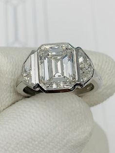 an emerald and diamond ring sits on a white cloth