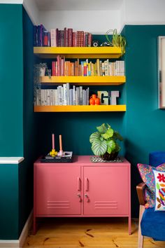 a living room with bookshelves and pink cabinet in the corner next to a blue chair