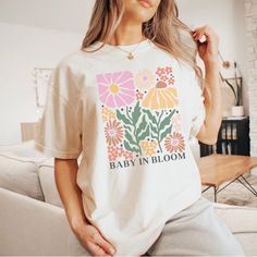 "Celebrate the journey of motherhood with our Baby In Bloom t-shirt! This adorable shirt is the perfect gift for your pregnant daughter or any expecting mom. With its charming design, it makes for a heartwarming pregnancy reveal or baby announcement idea. Let your loved one proudly display their blossoming journey into motherhood with this thoughtful and stylish shirt. Our Garment-Dyed Heavyweight t-shirts are relaxed and UNISEX sized.  A great go to shirt for those who appreciate a structured f Cute Maternity T-shirt With Graphic Print, Cute Maternity Graphic Print T-shirt, Cute Maternity Cotton T-shirt, Casual White Maternity T-shirt, Maternity Graphic Tee With Short Sleeve, White Graphic Maternity T-shirt, Maternity Family Matching T-shirt With Graphic Print, Maternity T-shirt With Graphic Print And Relaxed Fit, Maternity Short Sleeve T-shirt For Spring