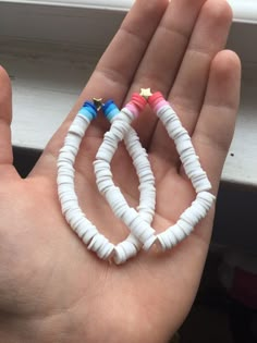 two small white and blue bracelets are held in someone's hand by a window