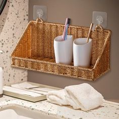 two cups and toothbrushes are in a basket hanging on the wall above a sink