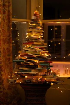 a christmas tree made out of books sitting in front of a window with lights on it