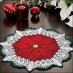 a crocheted doily with a red flower on it sitting on a table