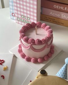 a pink birthday cake sitting on top of a table next to books and a teddy bear