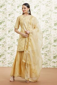 Gold cotton kurta with mixed pattern, all over gota embroidery and cut work border details. Paired with gharara with butti pattern, contrast resham work and dupatta with floral foil print.
Components: 3
Pattern: Embroidered and Printed
Type Of Work: Resham, Gota Work and Foil Print
Neckline: Round Neck
Sleeve Type: Half Sleeves
Fabric: Cotton, Dupatta: Organza, Lining: Cotton
Color: Gold
Other Details: 
Cut work hem details
Front loop buttons
Side slits on kurta
Attached lining
Gharara Closure: Sharara With Chikankari Embroidery And Straight Kurta In Chanderi, Gold Chikankari Embroidery Chanderi Sharara, Festive Chikankari Embroidered Dola Silk Sharara, Transitional Gold Sharara With Dori Work, Festive Sharara With Chikankari Embroidery In Raw Silk, Semi-stitched Sharara With Chikankari Embroidery, Festival Sharara With Chikankari Embroidery In Raw Silk, Chikankari Embroidered Raw Silk Sharara For Festivals, Festive Chanderi Sharara With Chikankari Embroidery