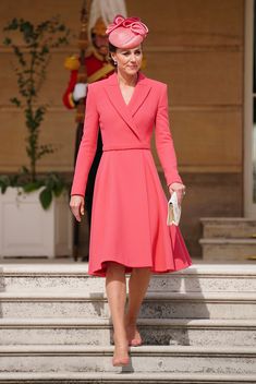 a woman in a pink dress and hat is walking down the steps