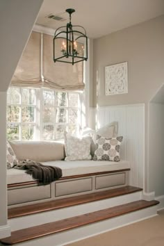 a window seat with some pillows on it and a light fixture hanging from the ceiling