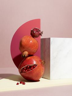 two pomegranates are stacked on top of each other in front of a pink background