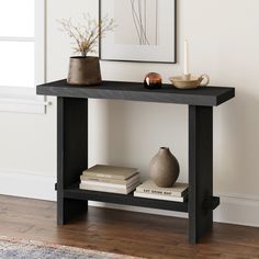 a black table with books and vase on it next to a white wall in a living room