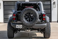 the rear end of a black jeep parked in front of a garage