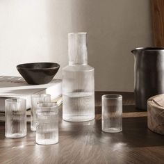 several clear glass vases and glasses on a wooden table next to a black bowl